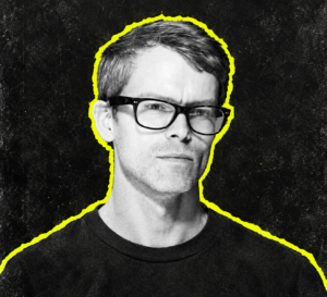 Surgeon wearing glasses in a black-and-white head-and-shoulders portrait with a yellow outline.