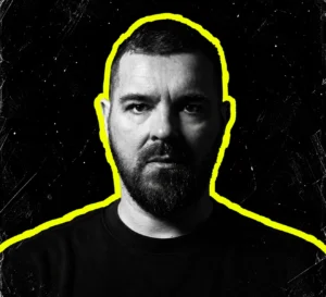 Speedy J in a dark shirt, pictured in black and white with a yellow outline against a charcoal background.